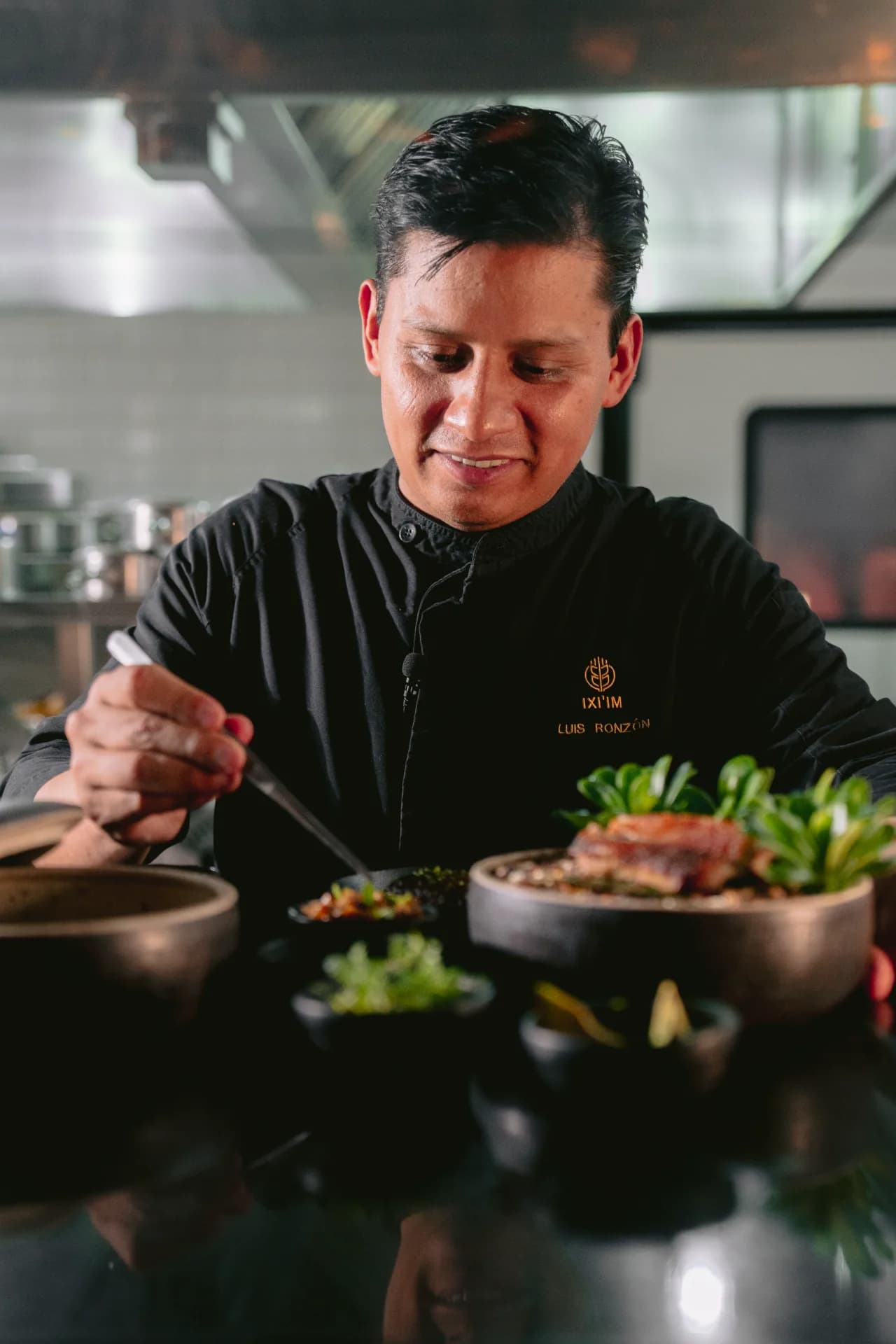 El chef Luis Ronzón emplatando en cuencos de barro oscuro en la cocina de Olivea, Valle de Guadalupe